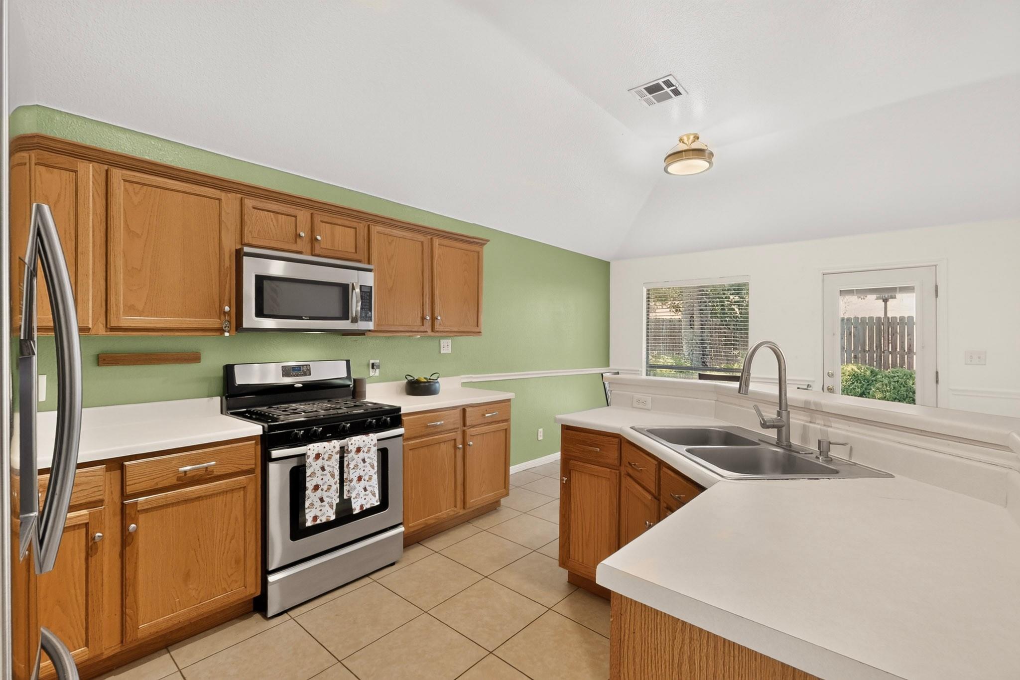 Kitchen with oak cabinets, white counters, a black range, and a double-basin sink by the back door.