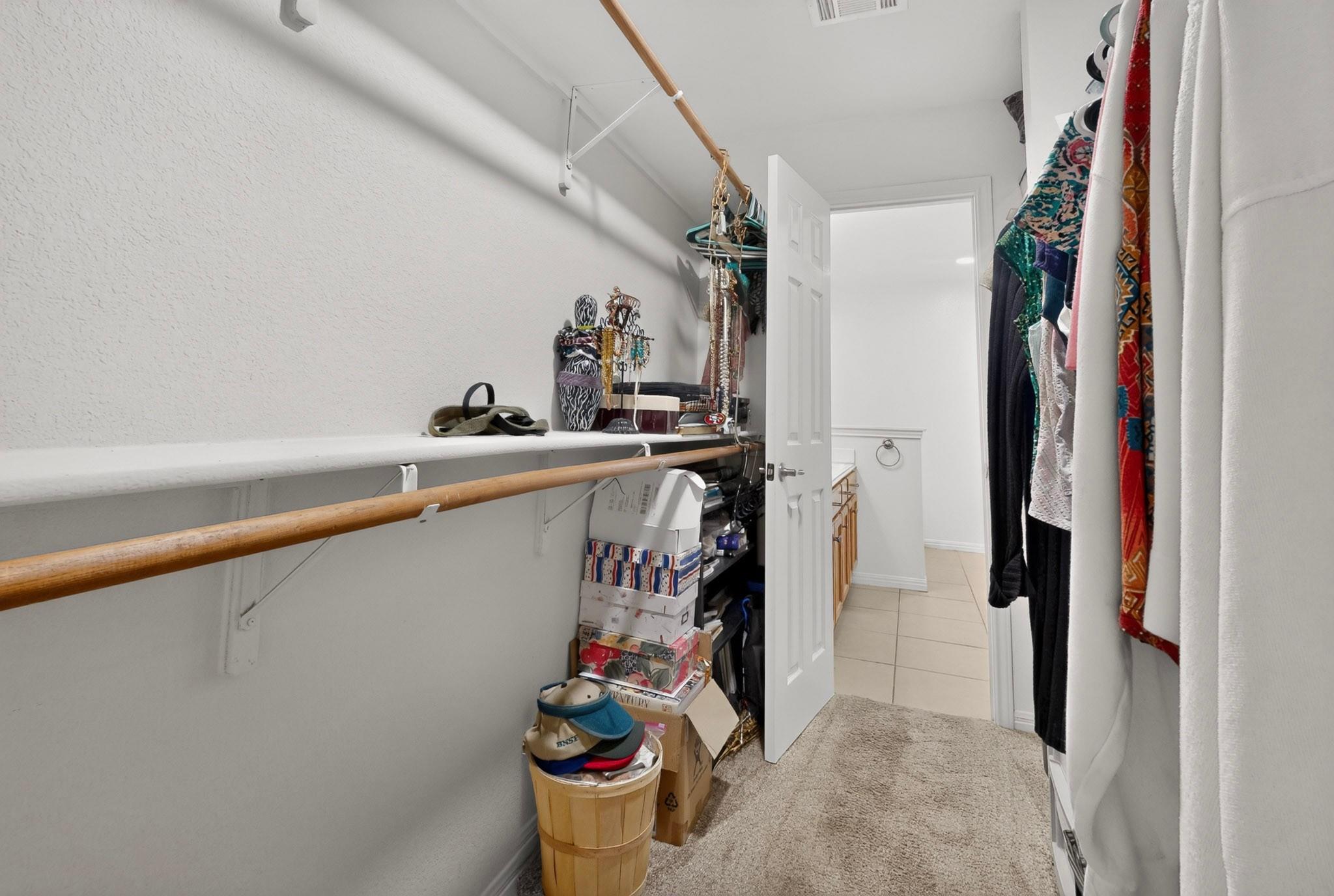 Walk-in closet with hanging clothes, a long wooden clothing rod, and stacked storage boxes.