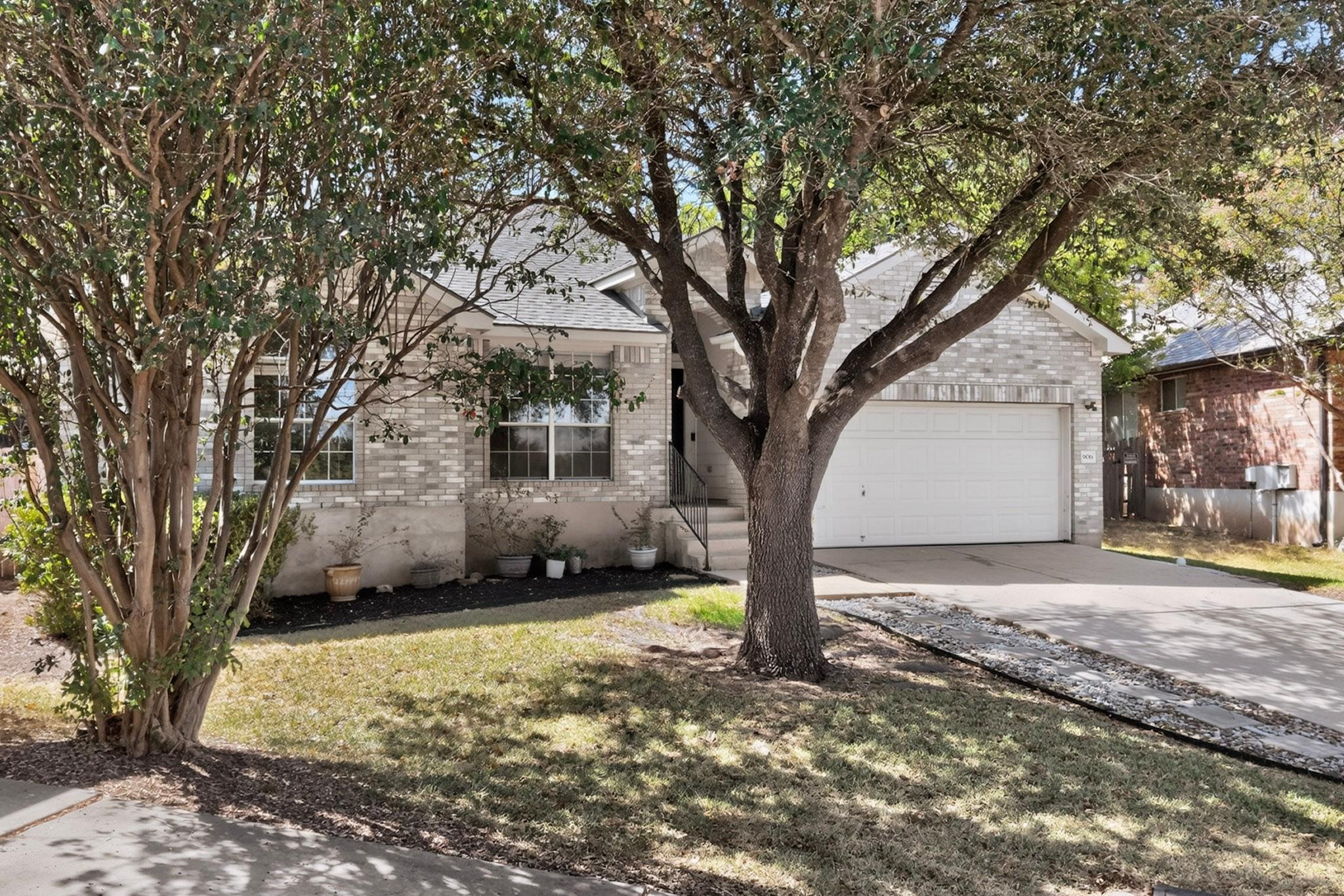 Light brick house with a two-car garage, shaded by mature trees.