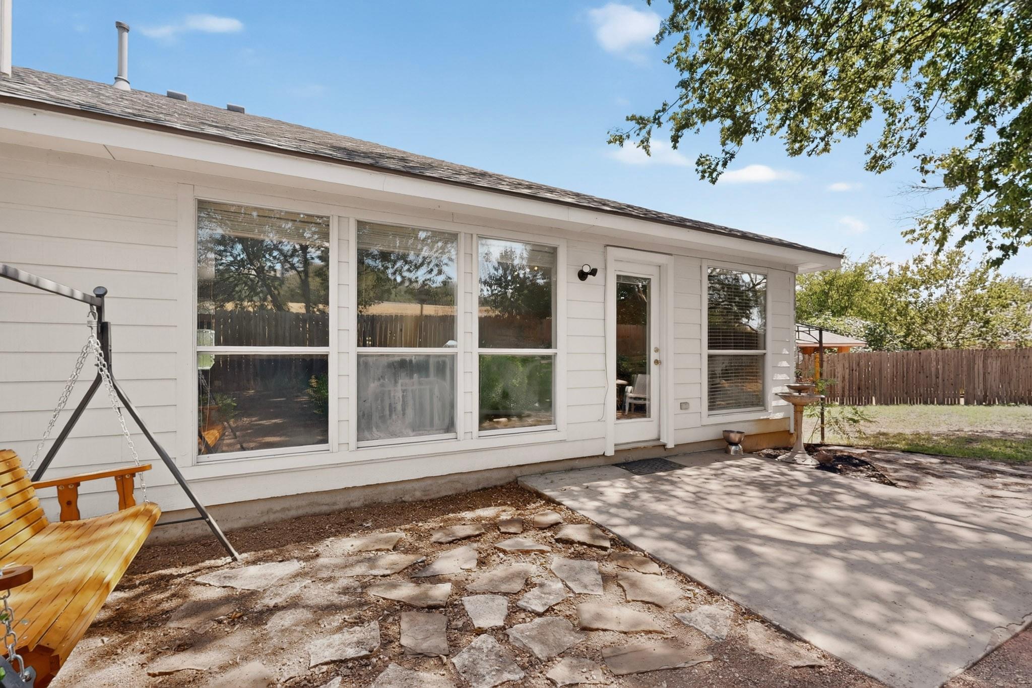 Rear of a white home with large windows, a paved patio, flagstone ground, and a wooden porch swing.
