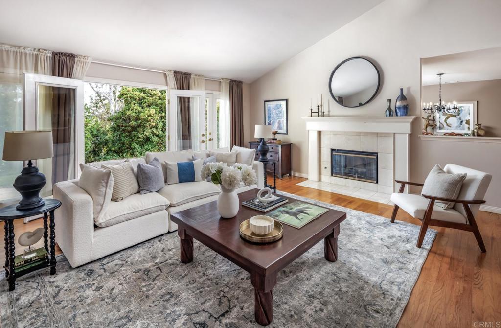 Living room with a tiled fireplace, white seating, and French doors overlooking greenery.