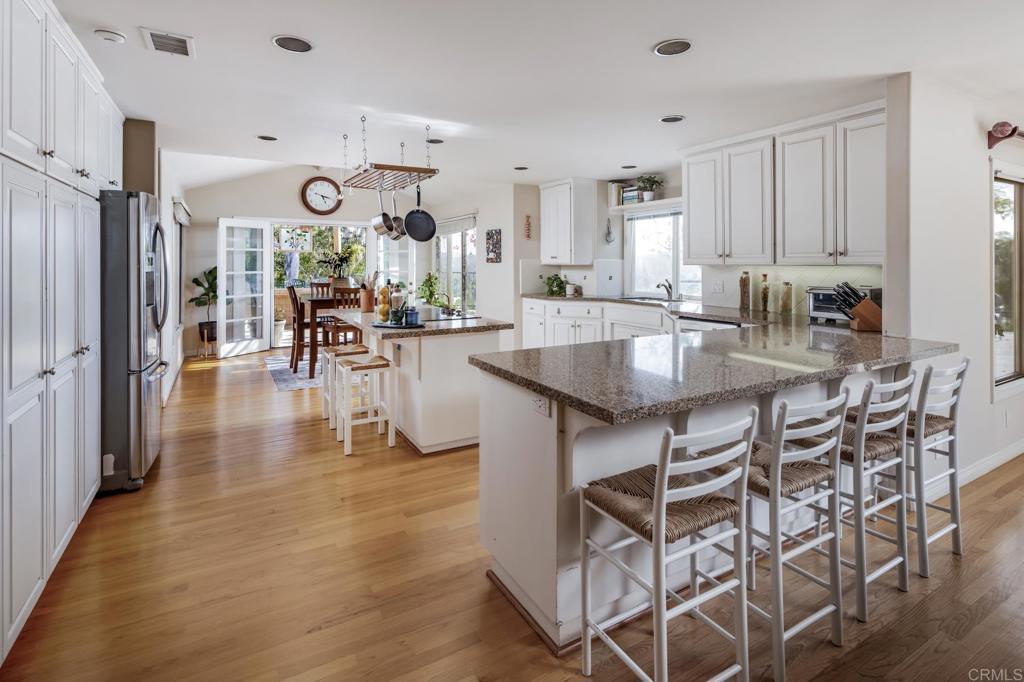 Bright kitchen with a granite island, white cabinetry, bar stools, and hardwood floors.