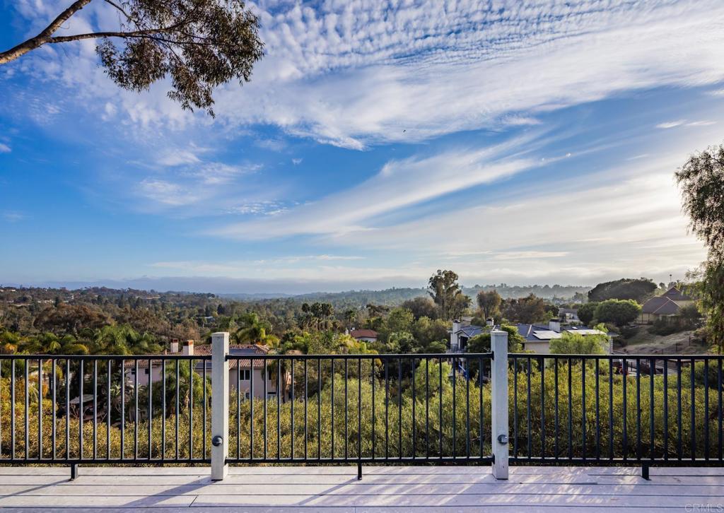 Deck railing overlooks homes and rolling hills beneath a broad, cloud-streaked sky.