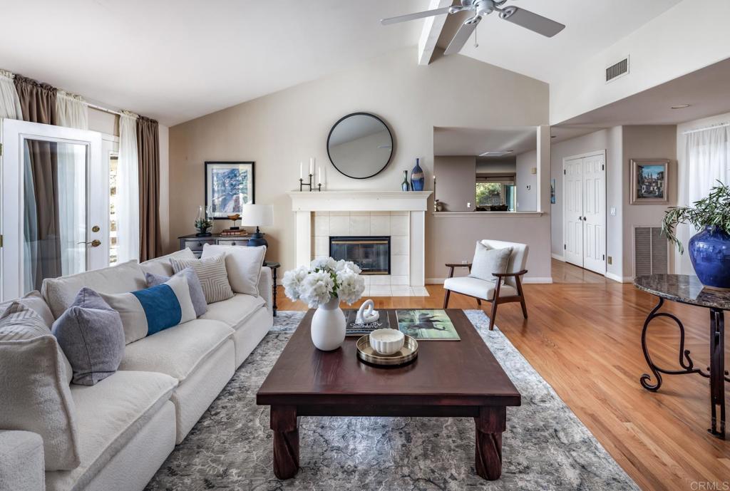 Furnished living room with a fireplace, round mirror, white sofa, and hardwood floors.