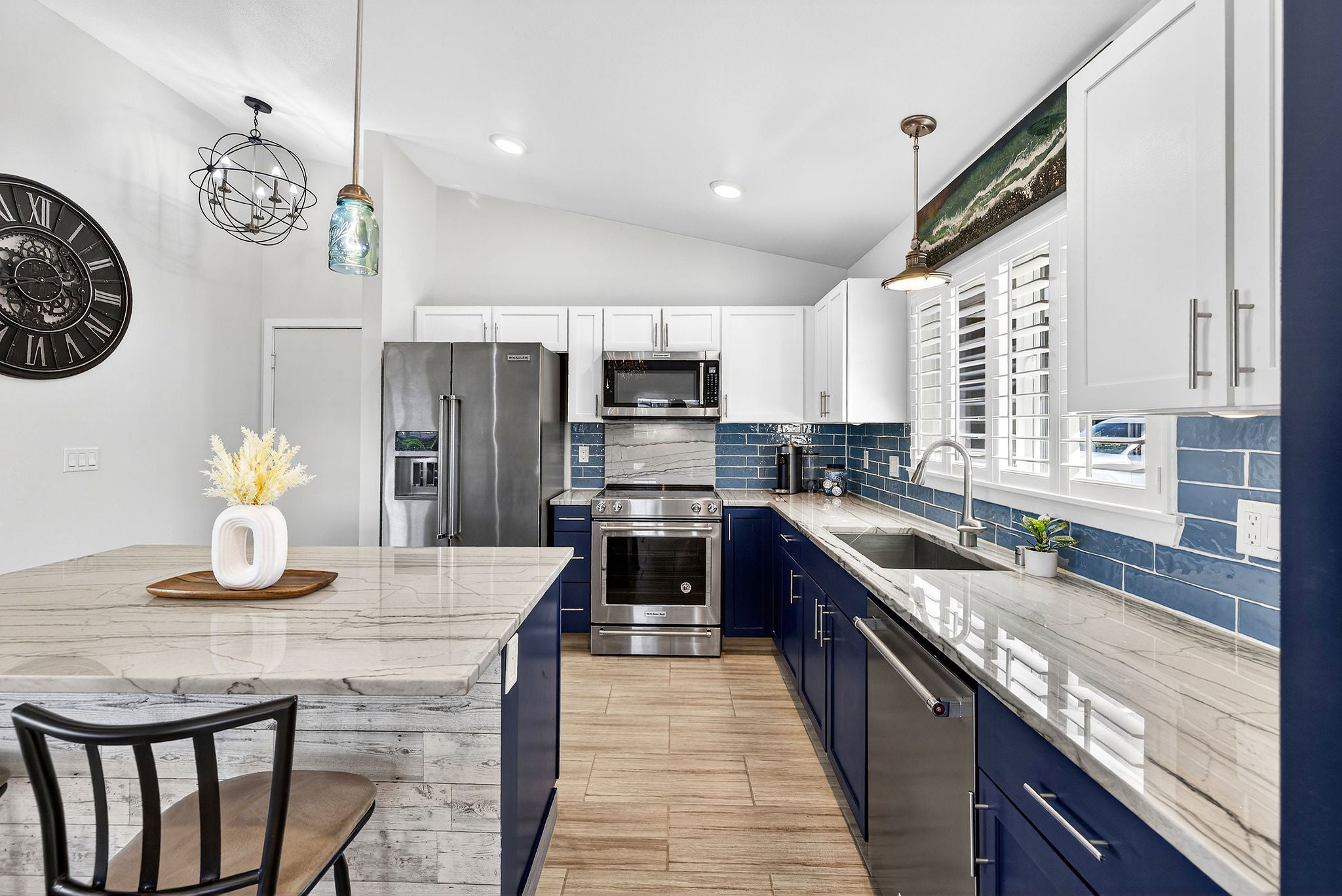 Bright kitchen with navy cabinets, blue tile backsplash, marble-look counters, and stainless steel appliances.