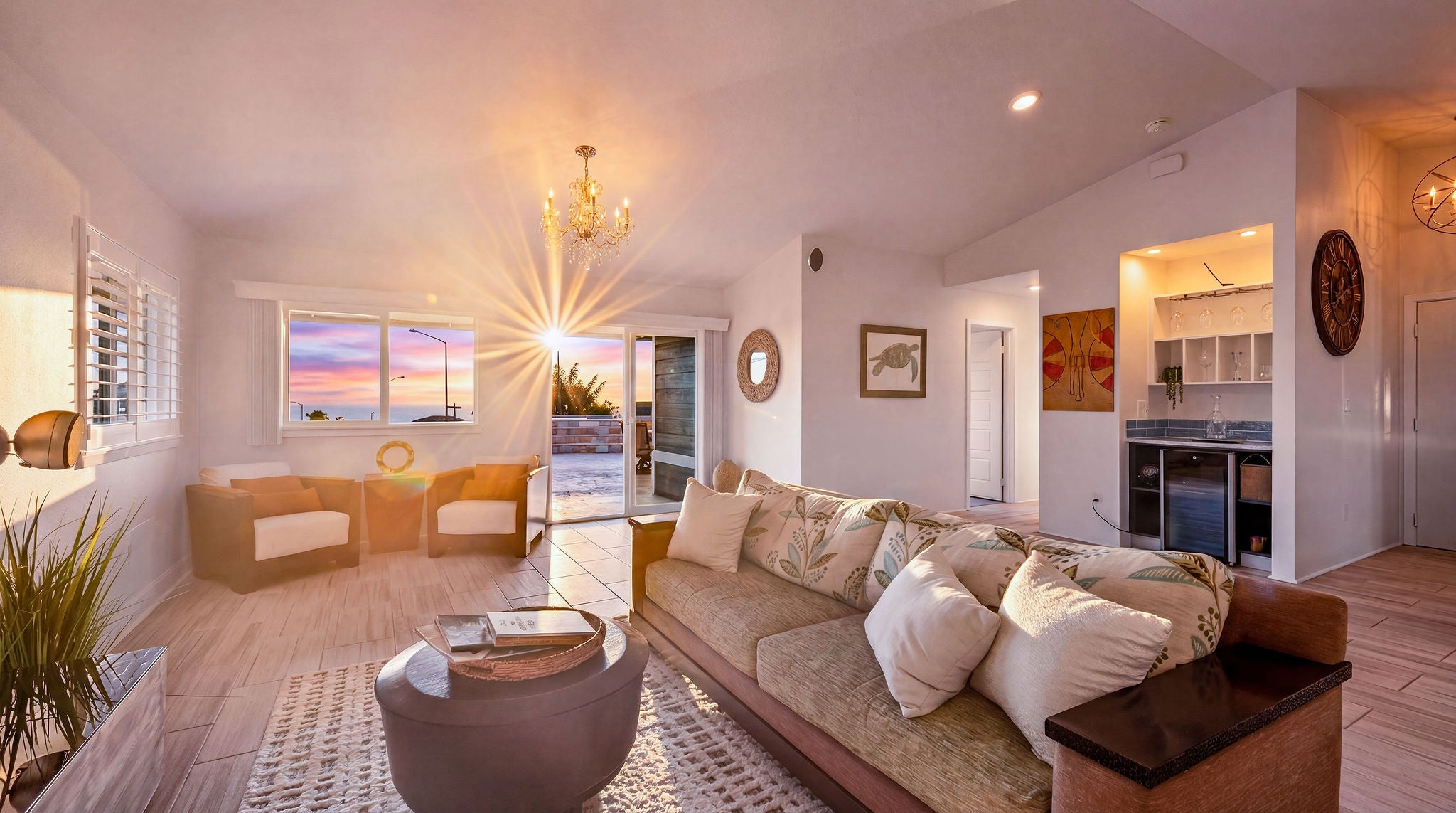 Living room with a patterned sectional and ocean sunset visible through wide windows.