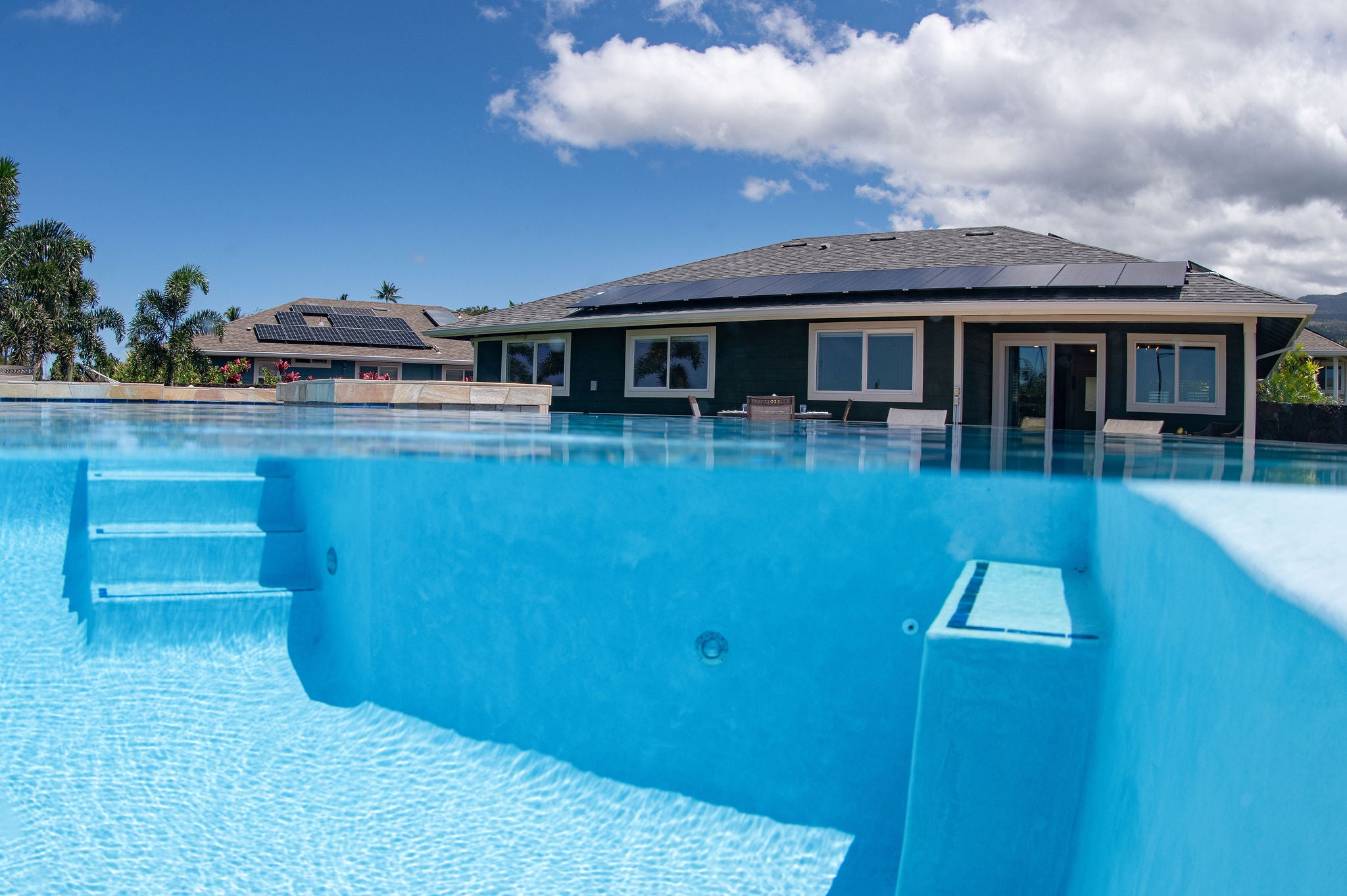 Swimming pool with submerged steps and shallow ledge in front of a solar-powered home.