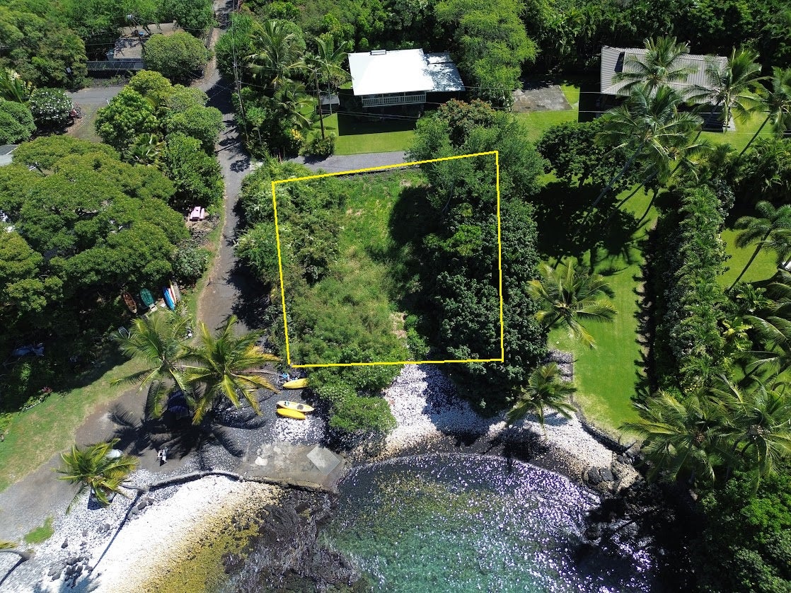 Aerial view of a yellow-outlined vacant lot beside a rocky shoreline and clear water.