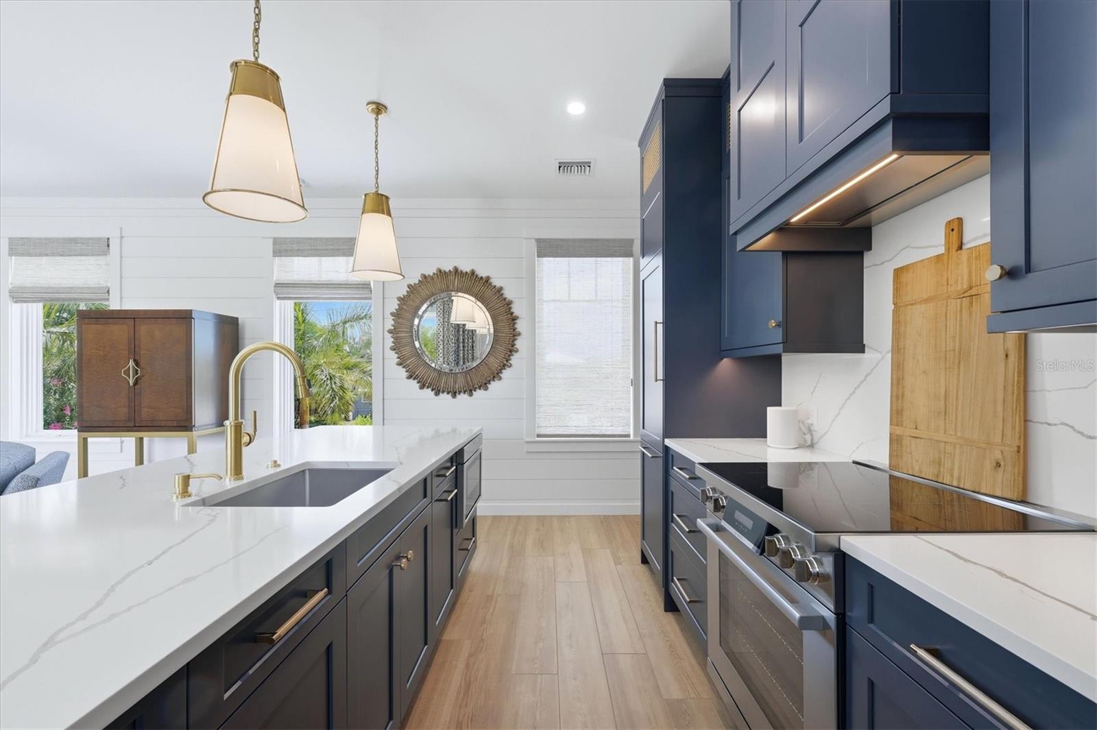 Kitchen with navy cabinetry, white stone counters, a large island, gold faucet, and stainless steel appliances.
