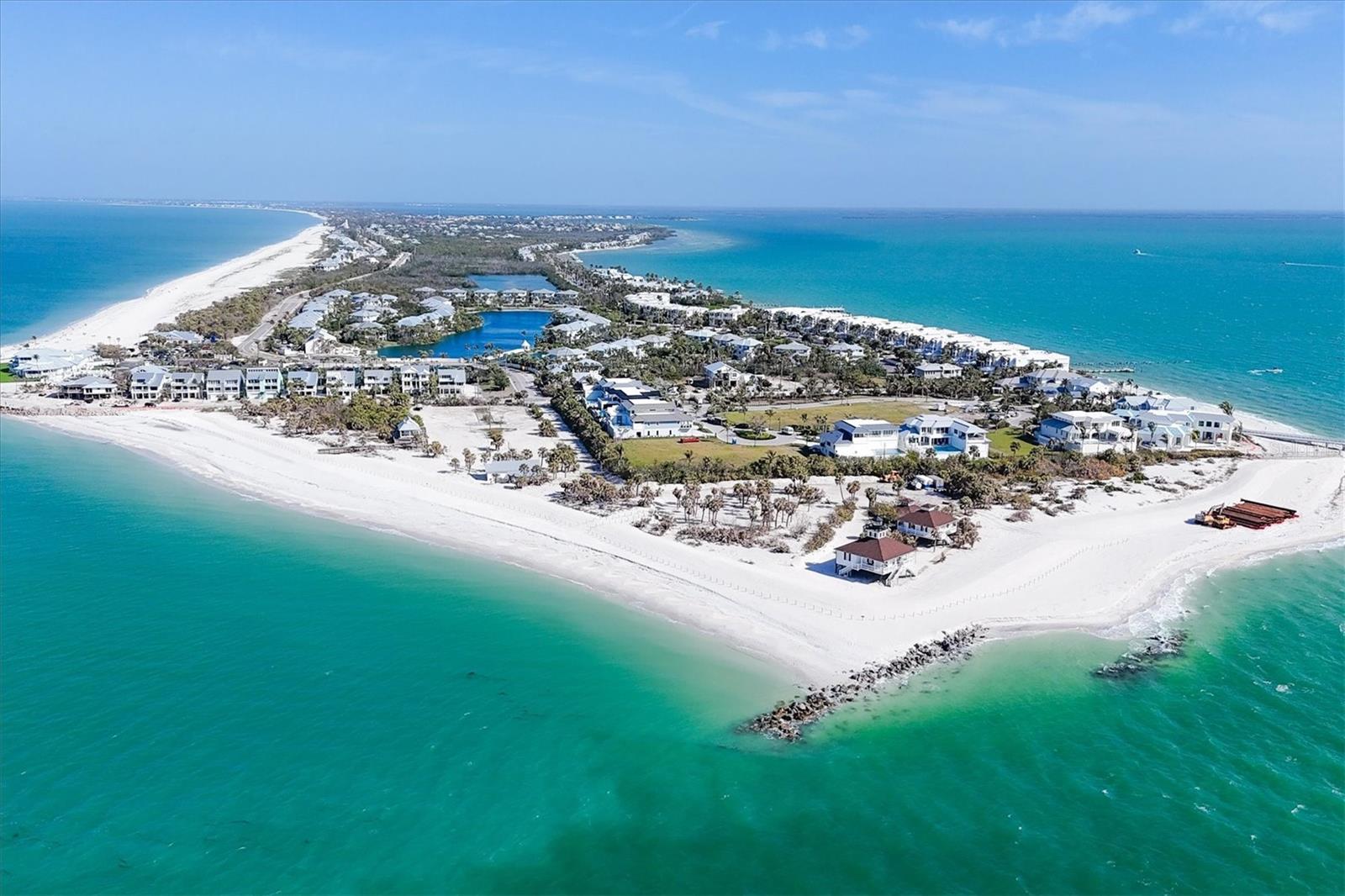 Aerial view of a coastal peninsula with white-sand beaches, homes, and turquoise water.