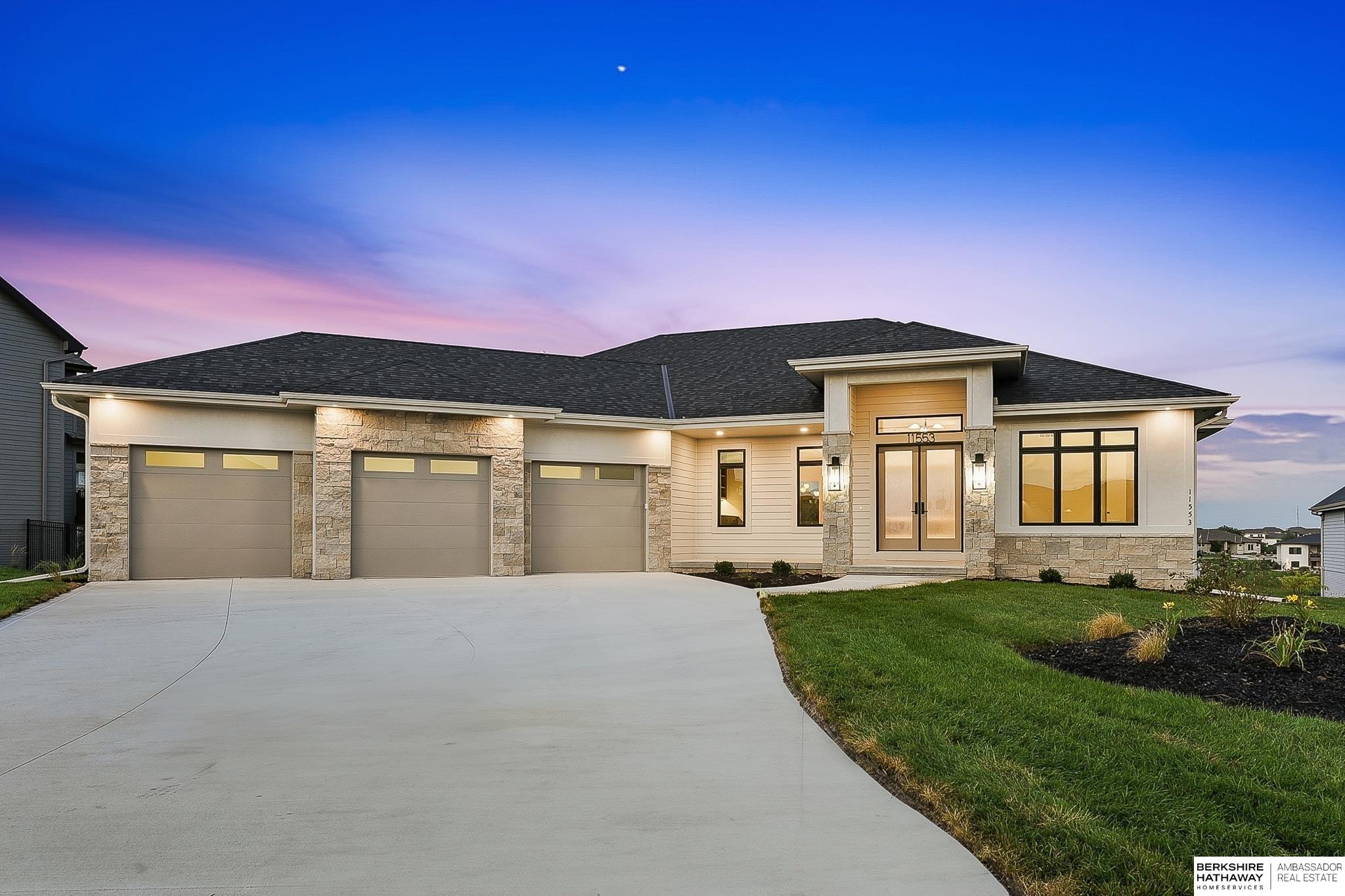 Single-story home with a three-car garage, stone accents, and a wide driveway at dusk.
