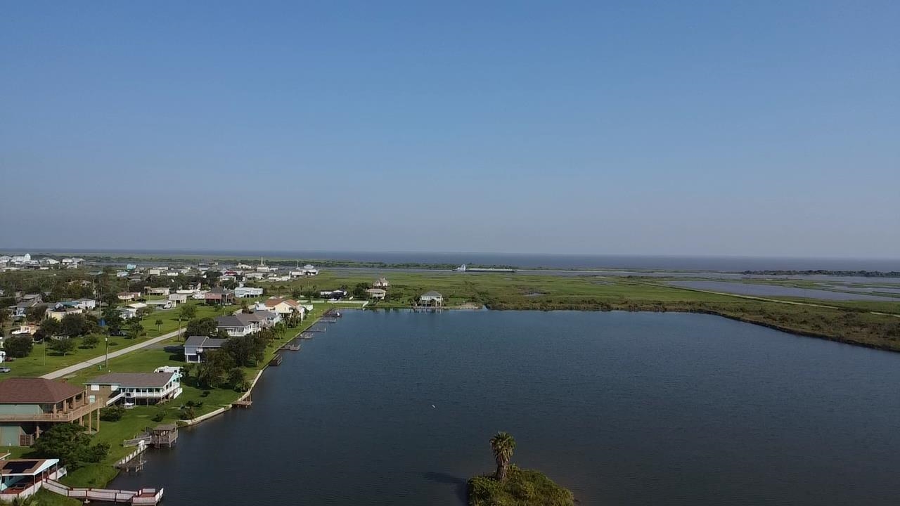 Waterfront homes and docks beside a broad waterway, with coastal marshland in the distance.