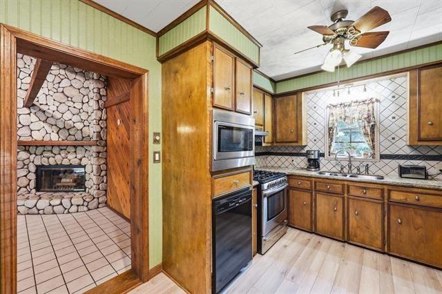 Kitchen with wood cabinets and built-in ovens, beside a stone fireplace through the doorway.