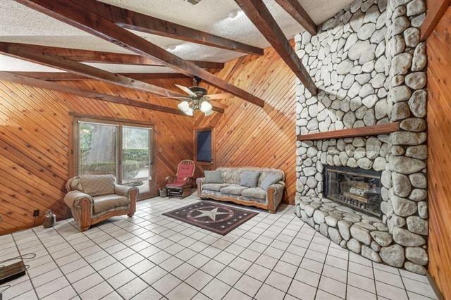 Living room with a stone fireplace, vaulted wood ceiling, and tiled floor.