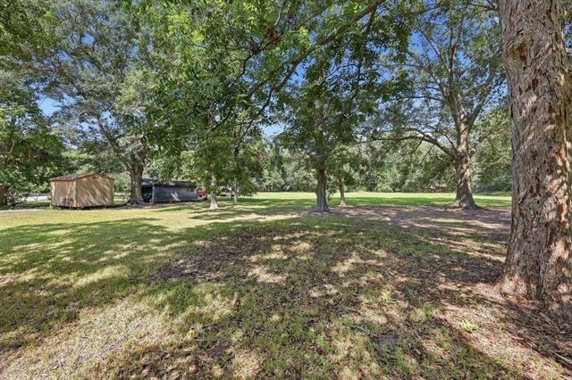 Grassy yard shaded by mature trees, with a small shed and outbuilding near the back.
