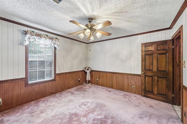 Empty bedroom with wood paneling, striped wallpaper, pale carpet, and a ceiling fan.