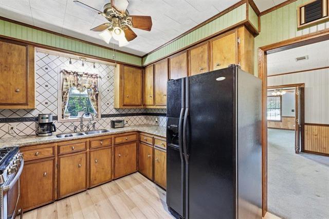 Kitchen with wood cabinets, black refrigerator, tiled backsplash, and a window above the sink.
