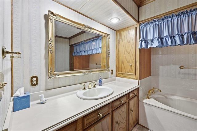 Bathroom with a white bathtub, wood vanity, and ornate gold-framed mirror.