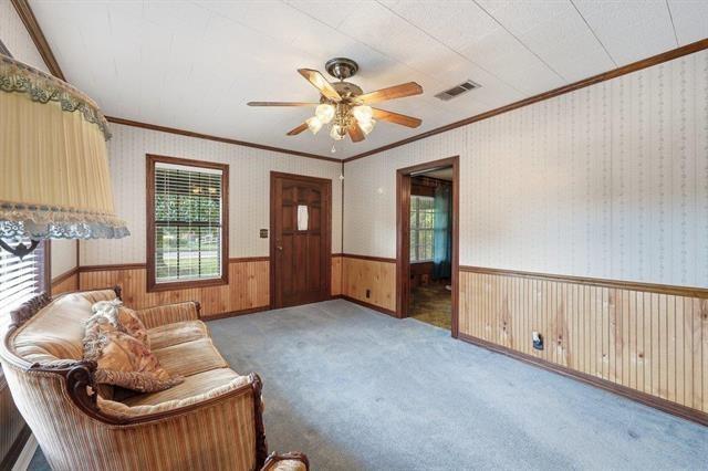 Living room with wood paneling, patterned wallpaper, blue carpet, and a ceiling fan.