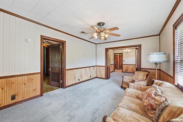 Living room with wood wainscoting, pale blue carpet, and wide doorways to adjoining rooms.