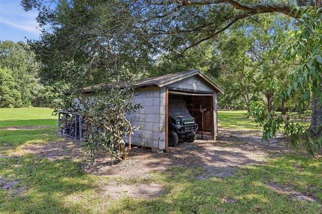Detached storage shed with an open doorway and a utility vehicle beneath mature trees.