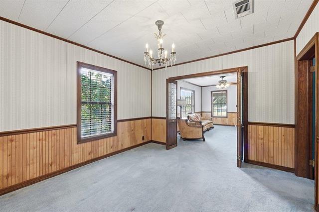 Carpeted room with wood wainscoting and a chandelier, opening into a sitting room with armchairs.