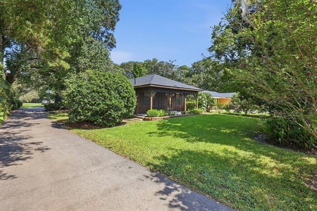 Single-story home behind a green lawn and mature trees, with a paved driveway.