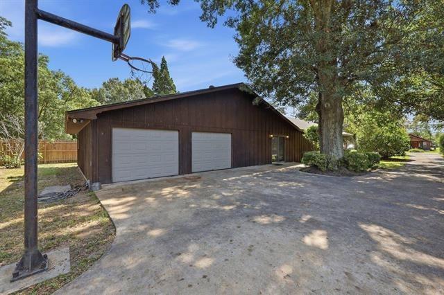Brown garage building with two doors, a broad concrete driveway, and a basketball hoop.