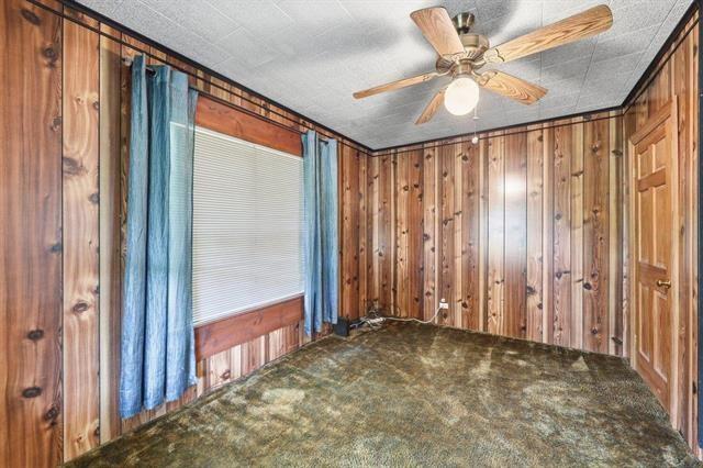 Unfurnished wood-paneled room with blue curtains, patterned carpet, and a ceiling fan.