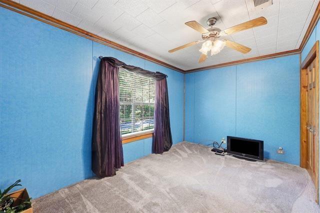 Empty blue bedroom with gray carpet, dark window curtains, and a ceiling fan.