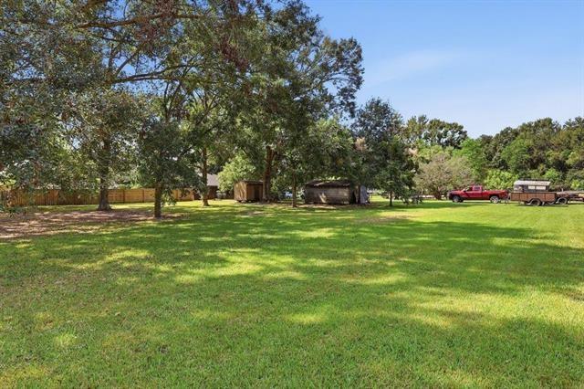 Spacious grassy yard shaded by mature trees, with outbuildings and a pickup with trailer.