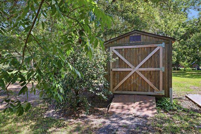 Wooden backyard shed with an X-braced door among leafy trees.