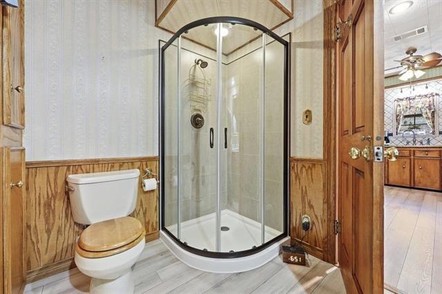 Bathroom with a curved glass shower, white toilet, and wood-paneled walls.