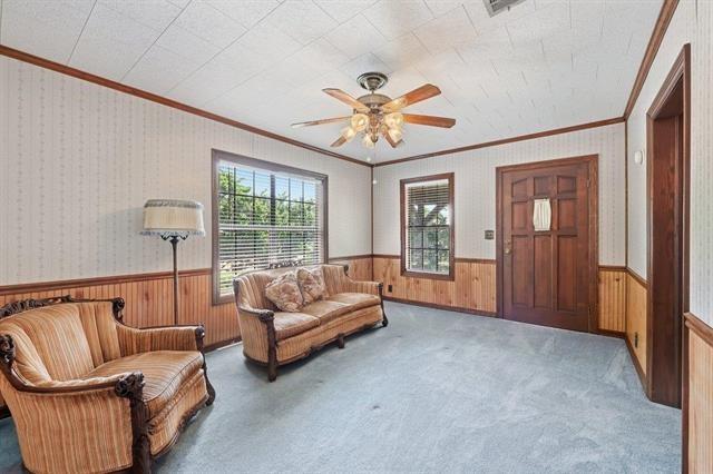 Living room with striped sofas, wood-paneled walls, pale blue carpet, and a ceiling fan.