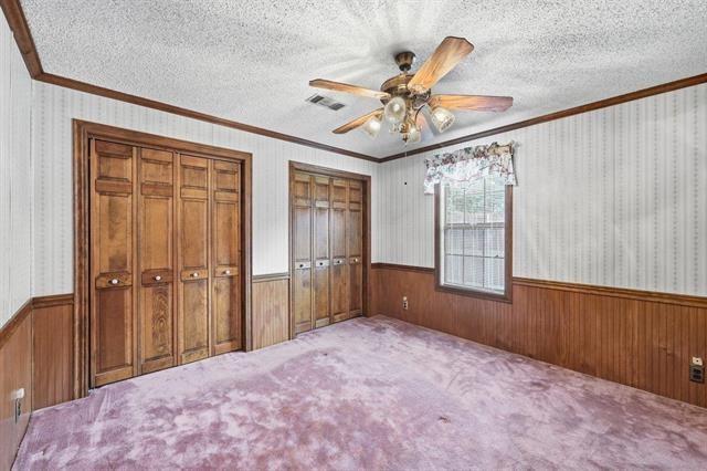 Vacant bedroom with wooden closet doors, mauve carpet, and a ceiling fan.