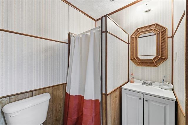 Bathroom with a white vanity, wicker-framed mirror, and shower curtain with a burgundy panel.