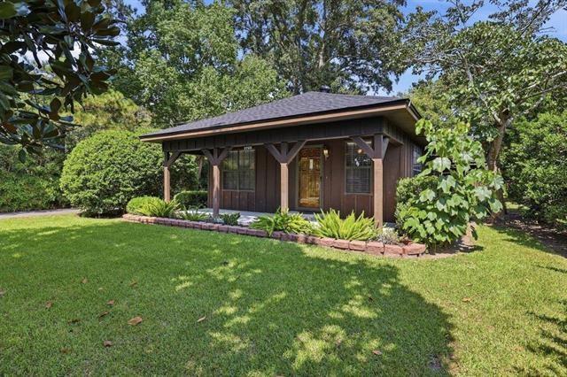 Single-story brown house with a covered porch, mature trees, and a broad front lawn.