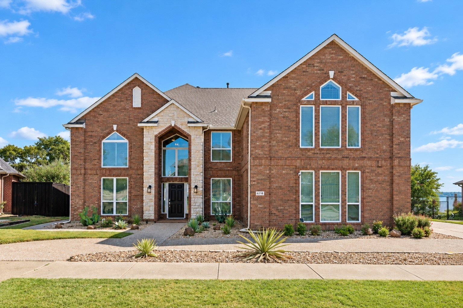 Two-story brick house with stone entry, tall windows, and landscaped desert-style yard.
