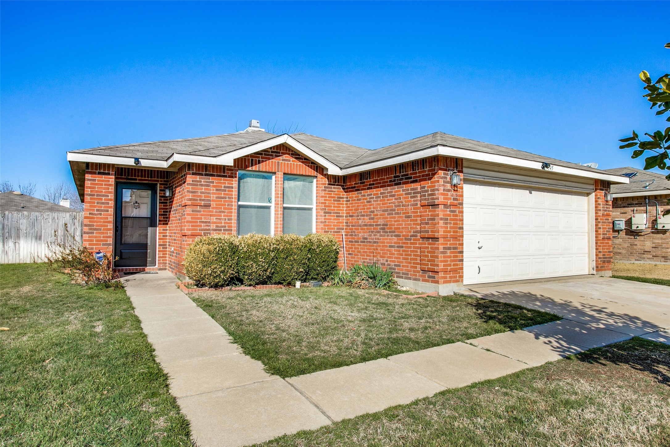 Single-story red-brick home with a white double garage and front lawn.
