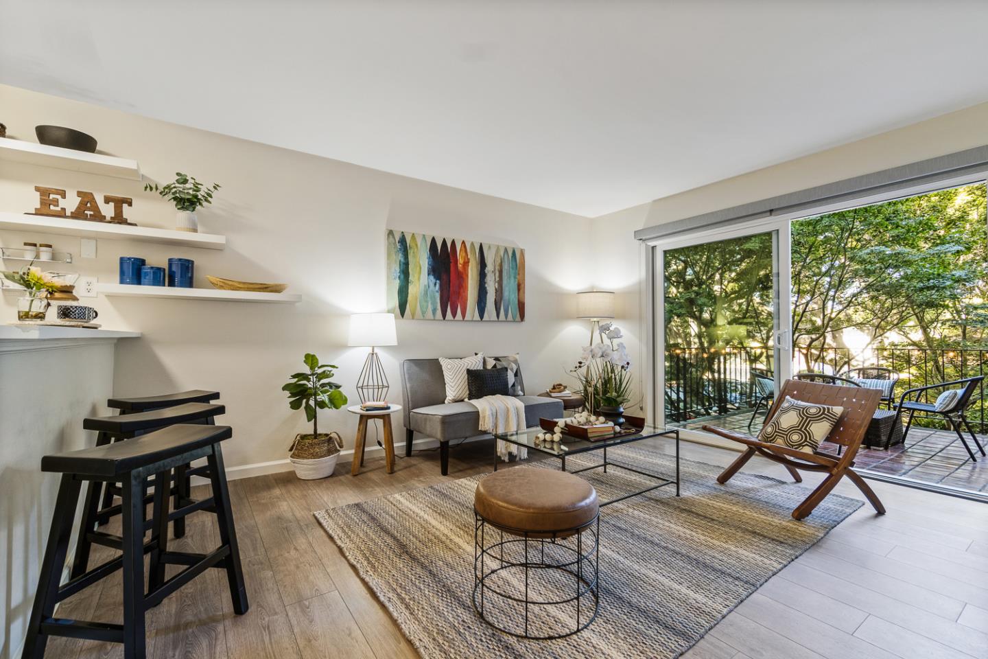 Staged living room with colorful surfboard artwork and sliding doors to a leafy balcony.