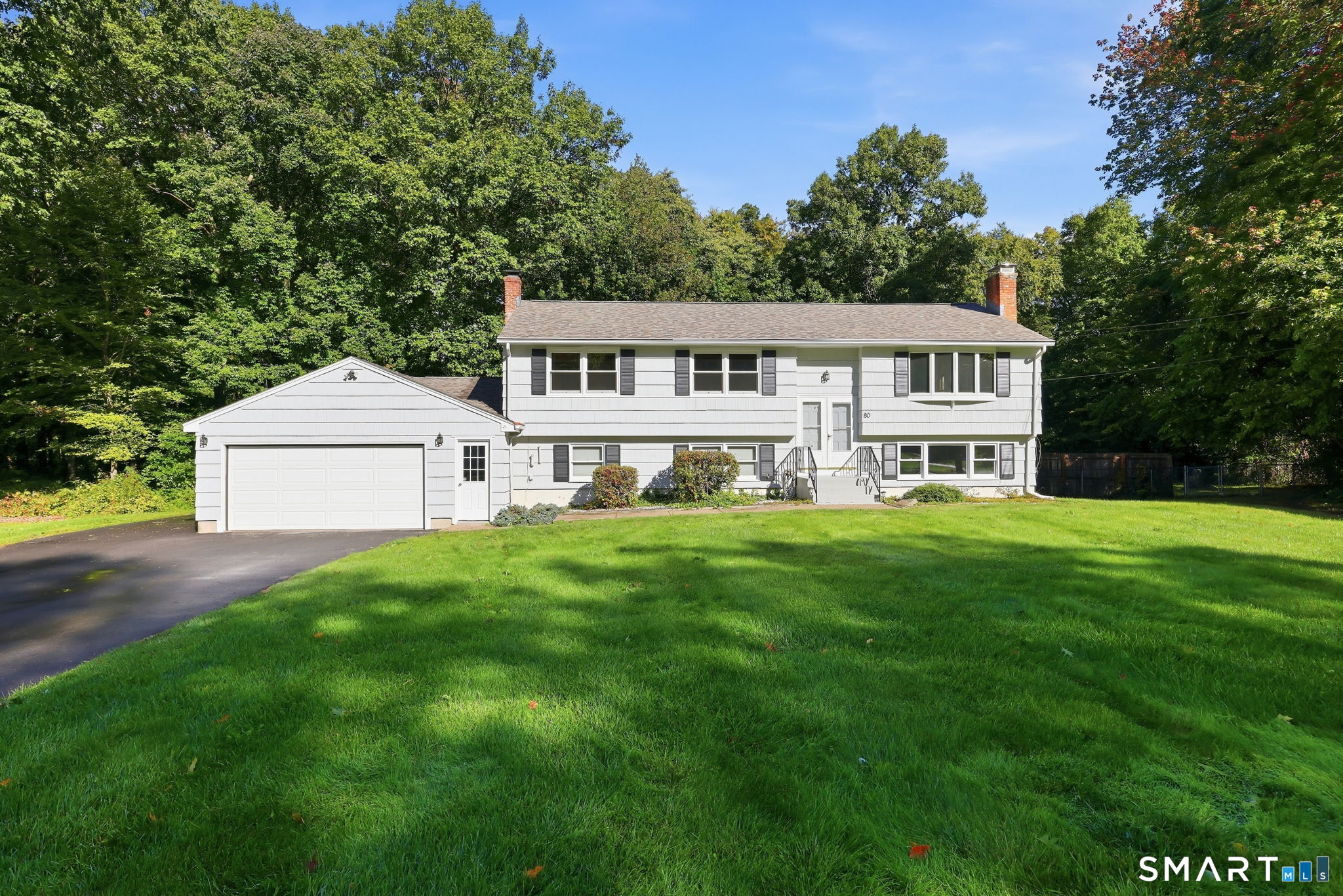 White split-level house with attached garage, broad lawn, and mature trees.