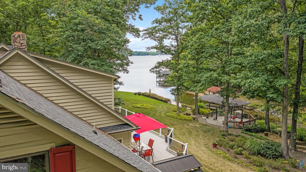 Elevated view of a lakeside home with a red-umbrella deck, wooded yard, and dock.
