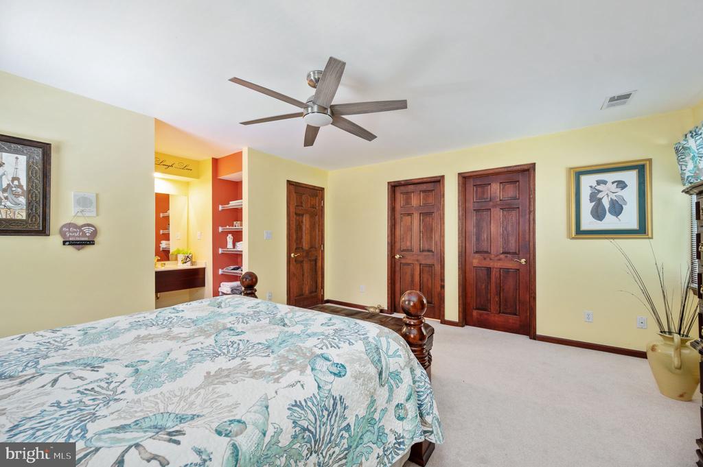 Bedroom with a floral bedspread, dark wood doors, ceiling fan, and open dressing area.