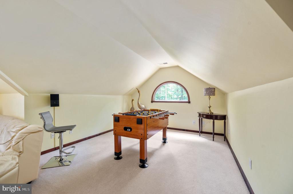 Furnished game room with a foosball table beneath a sloped ceiling and arched window.