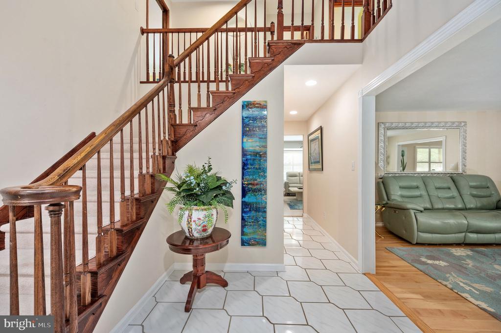 Entryway with a dark wood staircase, white geometric tile floor, and a potted plant beside the hall.