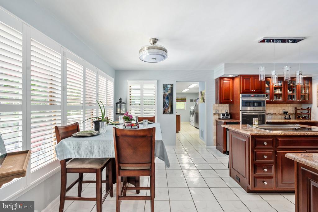 Kitchen and dining area with dark wood cabinetry, a granite island, and a table beside shuttered windows.