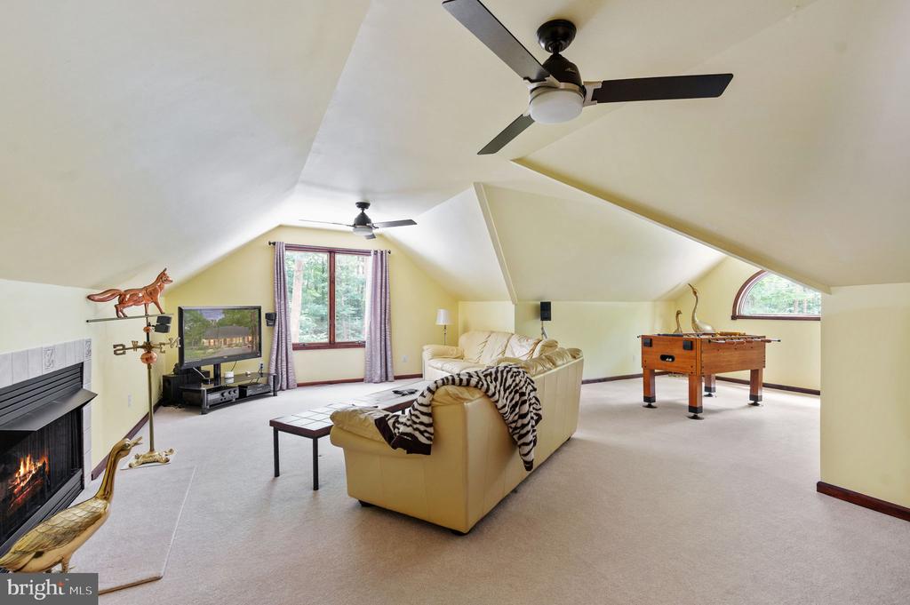 Furnished recreation room with vaulted ceiling, fireplace, sofa, and foosball table.