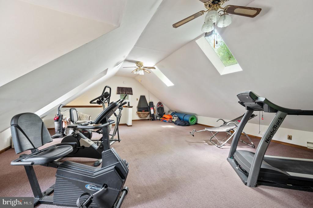 Attic exercise room with sloped ceilings, skylights, a treadmill, and stationary bike.