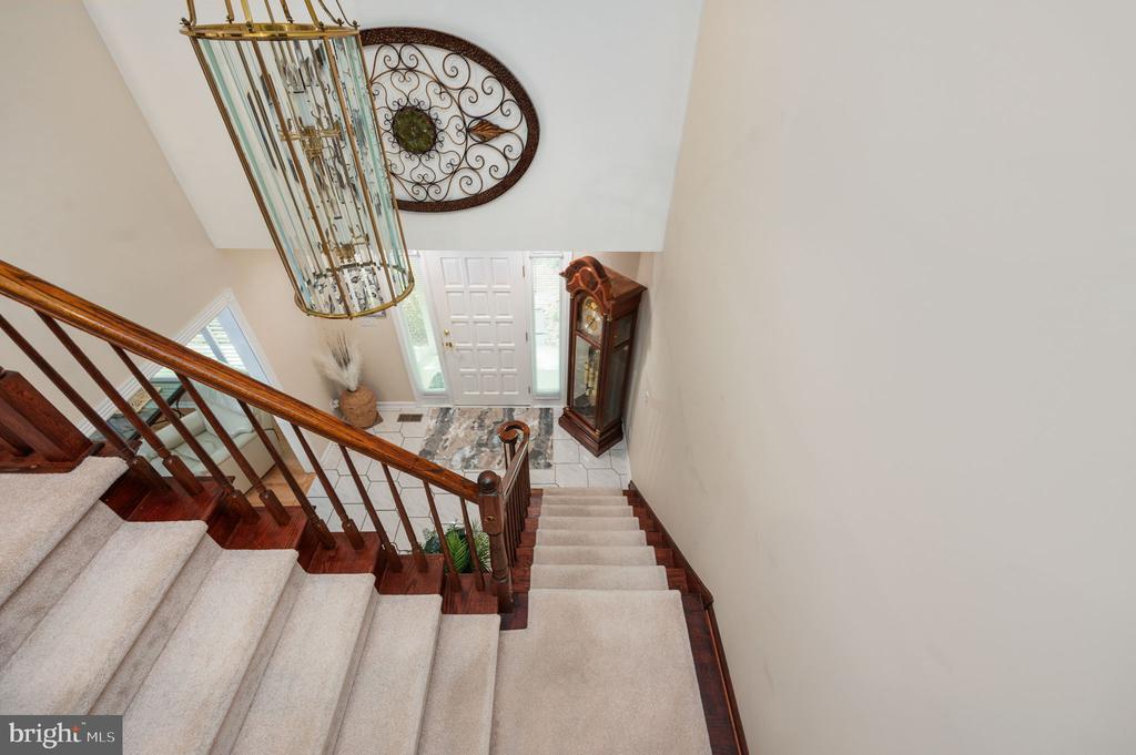 Carpeted staircase with polished wood railings overlooking the front entry and a grandfather clock.