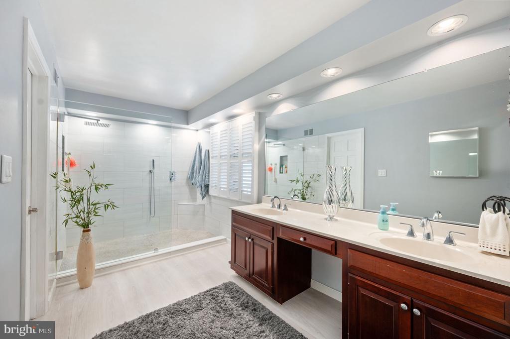 Bathroom with a glass walk-in shower and long double-sink vanity with dark wood cabinets.